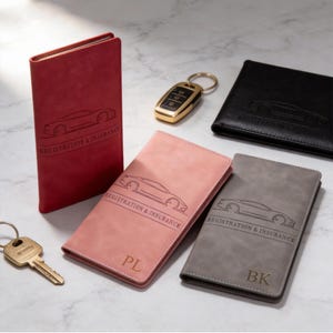 May include: A collection of car registration and insurance holders in red, pink, black, and gray. Each holder features a car outline and the text "REGISTRATION & INSURANCE". A gold car key and a key are also present.