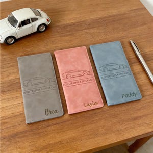 May include: Three personalized car registration and insurance holders in gray, pink, and blue. Each has a car outline and the text "Registration & Insurance." Names "Bria," "Layla," and "Paddy" are below.