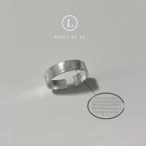 Könnte beinhalten: Ein verstellbarer Silberring mit strukturierter Oberfläche. Der Ring ist von Rings by Lu.