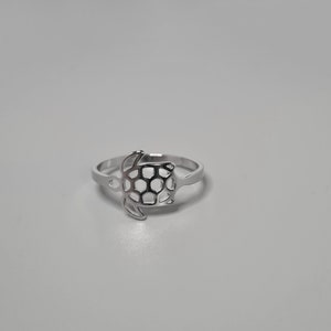 Puede incluir: Un anillo de plata con un diseño de tortuga recortada. El caparazón de la tortuga está detallado con un patrón de panal.