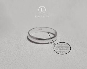 Puede incluir: Un anillo de banda de plata con el número 925 estampado en el interior. El anillo está sobre una superficie blanca.