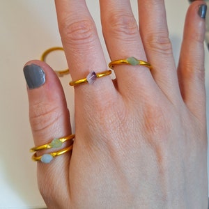 Könnte beinhalten: Drei goldene Ringe mit verschiedenen Edelsteinen. Die Ringe werden an den Fingern einer Person getragen.