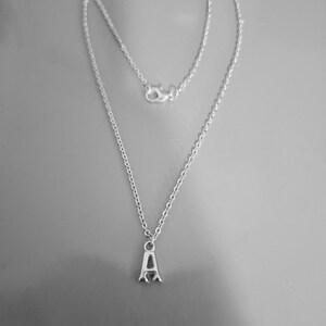 Puede incluir: Un collar de cadena de plata con un colgante de letra A de plata.
