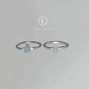 Könnte beinhalten: Zwei silberne Ringe mit jeweils einem hellblauen Stein. Die Ringe sind schlicht und zart, einer davon mit einer gehämmerten Oberfläche. Der Text "Rings by Lu" ist unter dem Bild zu sehen.