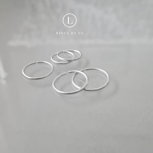 Könnte beinhalten: Fünf silberne Creolen in verschiedenen Größen. Die Ohrringe sind in einem Halbkreis auf einer weißen Oberfläche angeordnet. Der Text "Rings by Lu" ist oben in der Mitte des Bildes sichtbar.