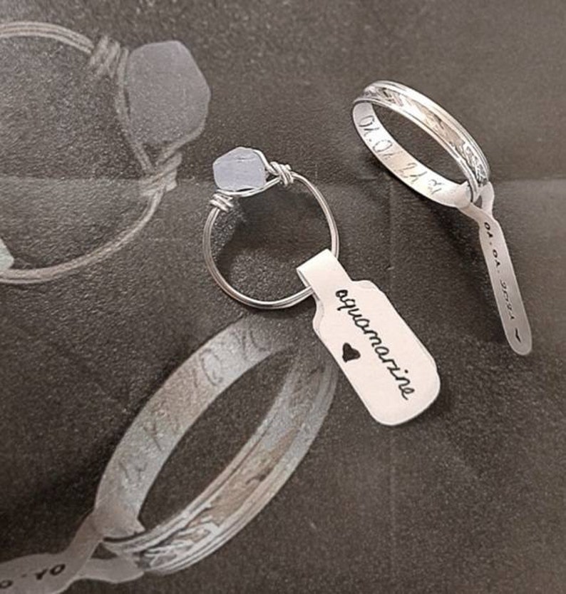 Puede incluir: Dos anillos de plata, uno con una piedra de aguamarina azul claro y una etiqueta que dice "aguamarina" con un s&iacute;mbolo de coraz&oacute;n. El otro anillo tiene una inscripci&oacute;n en la banda.