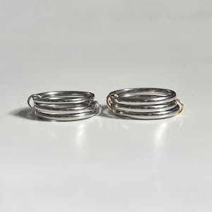 Könnte beinhalten: Zwei silberne Ringe mit mehreren Bändern. Ein Ring hat einen goldenen Akzent auf dem Band.