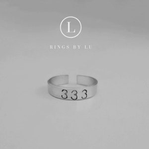 Könnte beinhalten: Ein silberner Ring mit der Zahl 333 eingraviert. Der Ring liegt auf einem weißen Hintergrund.