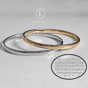 Puede incluir: Se muestran dos elegantes brazaletes, uno dorado y otro plateado. El brazalete dorado tiene un acabado pulido, mientras que el plateado tiene un aspecto elegante y liso. Un primer plano muestra una muestra de letras y números grabados.