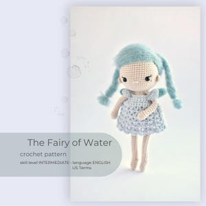 Puede incluir: Patrón de crochet para una muñeca de hada con cabello azul y un vestido azul claro. El patrón es para un nivel de habilidad intermedio y está escrito en inglés usando términos estadounidenses. La muñeca está de pie sobre un fondo blanco.