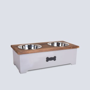May include: A grey wooden pet food stand with two stainless steel bowls. The stand has a bone-shaped cutout on the front.