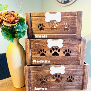 May include: Three wooden dog treat storage boxes with paw prints cutouts. The boxes are stacked from smallest to largest and labeled "Small", "Medium", and "Large".