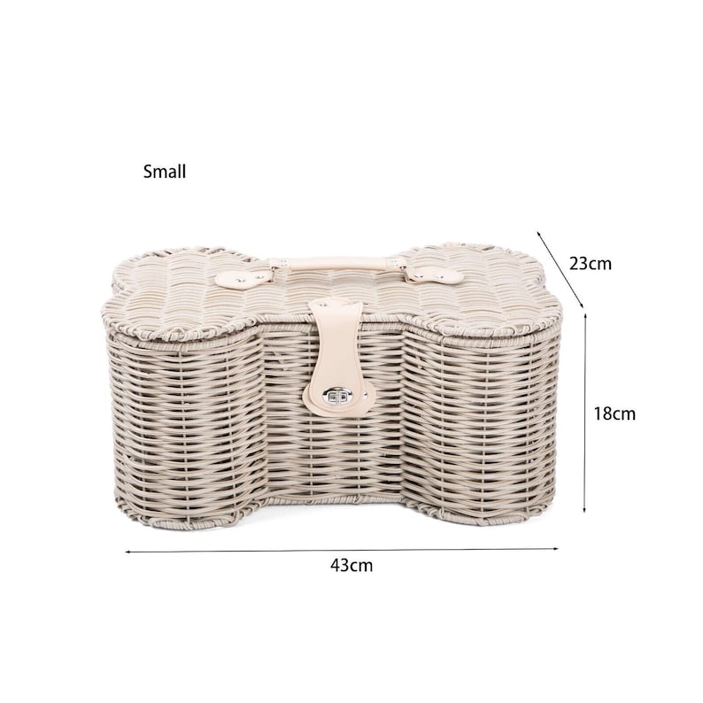 May include: A small bone-shaped wicker basket with a light beige finish, featuring a top handle and a central latch closure. The basket measures 43 cm in length, 23 cm in width, and 18 cm in height, providing a structured storage solution.