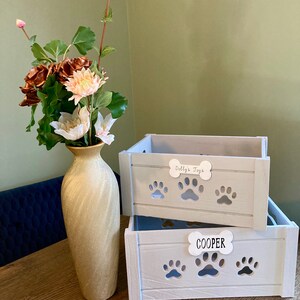May include: Two white wooden storage boxes with paw print cutouts. The top box has a white label that says "Dolly's Toys". The bottom box has a white label that says "COOPER".