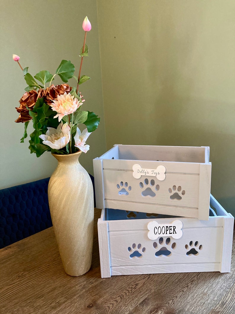 May include: Two white wooden storage boxes with paw print cutouts. The top box has a white label that says "Dolly's Toys". The bottom box has a white label that says "COOPER".