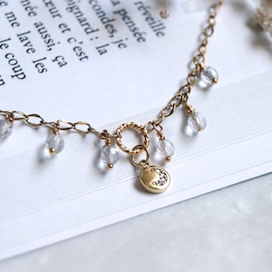 May include: A gold chain necklace with a crescent moon charm and clear crystal beads.