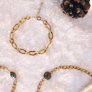 K&ouml;nnte beinhalten: Drei goldene Kettenarmb&auml;nder. Zwei der Armb&auml;nder haben einen Akzent aus dunkelgrauem Edelstein. Ein Armband hat einen tropfenf&ouml;rmigen Edelstein und das andere einen runden Edelstein.