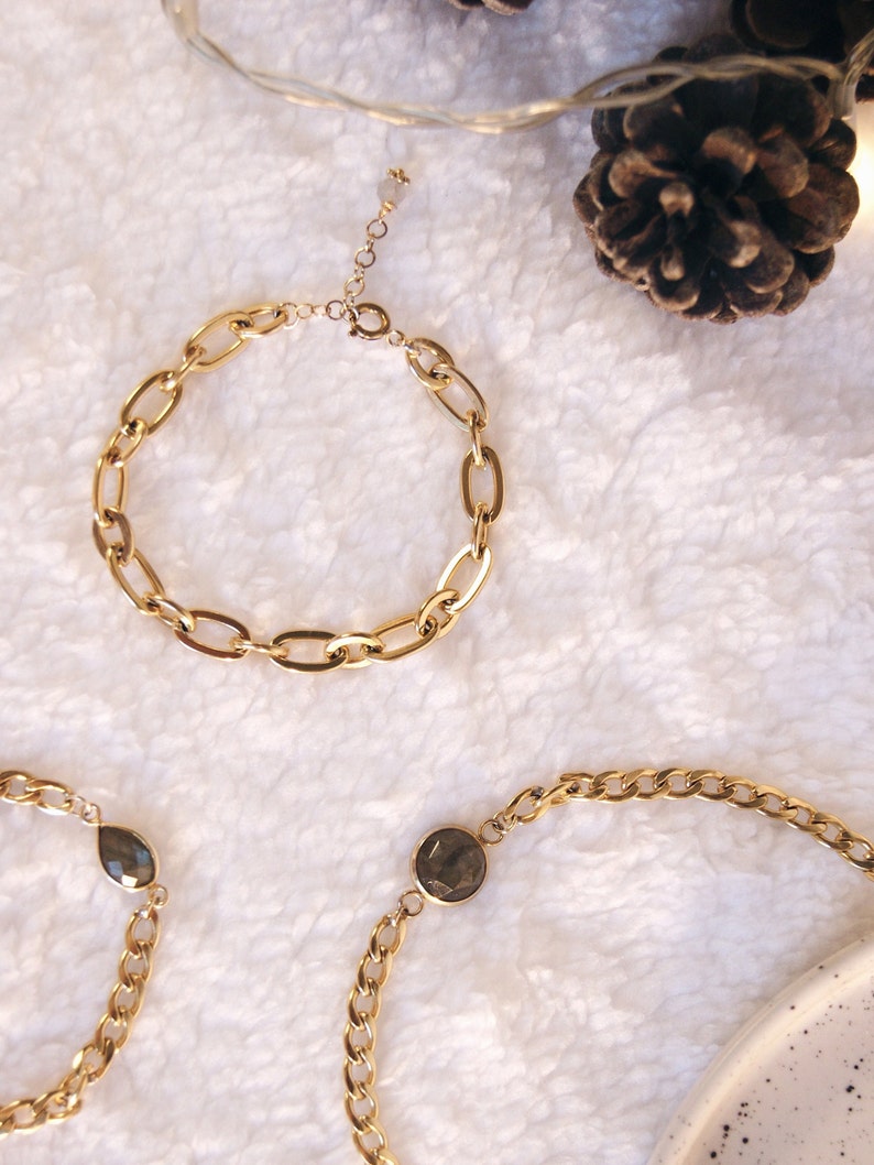 K&ouml;nnte beinhalten: Drei goldene Kettenarmb&auml;nder. Zwei der Armb&auml;nder haben einen Akzent aus dunkelgrauem Edelstein. Ein Armband hat einen tropfenf&ouml;rmigen Edelstein und das andere einen runden Edelstein.