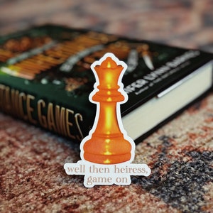 May include: A sticker of a chess queen with a bright orange glow and the text "well then heiress, game on".