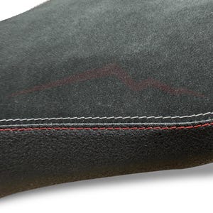 Puede incluir: Primer plano de una superficie negra texturizada con costuras blancas y rojas en el borde. Un dise&ntilde;o rojo descolorido es visible en la superficie, agregando un detalle sutil.