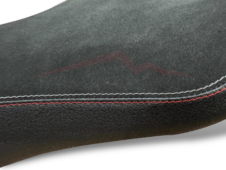 Puede incluir: Primer plano de una superficie negra texturizada con costuras blancas y rojas en el borde. Un dise&ntilde;o rojo descolorido es visible en la superficie, agregando un detalle sutil.