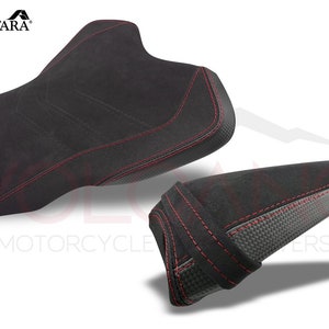 May include: A pair of black motorcycle seat covers with red stitching. The larger seat cover has a textured surface and the smaller seat cover has a carbon fiber look.