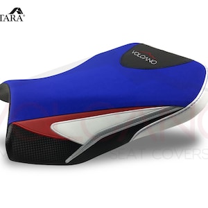 May include: A blue, white and black motorcycle seat cover with the word "VOLCANO" printed on it. The seat cover is made of Alcantara fabric.