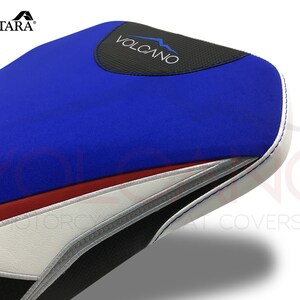 May include: Blue, red, white and black motorcycle seat cover with the word "VOLCANO" in white text on a black background.