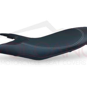 Puede incluir: Funda de asiento de motocicleta negra con costuras blancas. La funda del asiento tiene una forma ligeramente curvada y una textura lisa, similar al cuero.