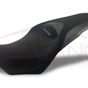 May include: Black motorcycle seat cover with blue stitching and a gray textured panel with the word "VOLCANO" printed on it.