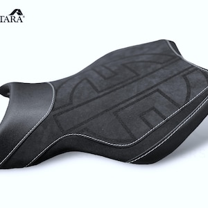 Può includere: Sella da moto nera con un inserto in tessuto Alcantara grigio e cuciture bianche. L'inserto in tessuto presenta un motivo geometrico.