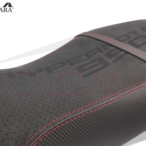 May include: Black motorcycle seat with red stitching and a perforated leather surface. The seat has the text "MOTO CORSE" embossed on the surface.