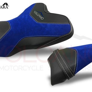 May include: A set of two motorcycle seat covers in blue and black. The covers are made of Alcantara fabric and have a carbon fiber look. The larger cover has the word "VOLCANO" printed on it.
