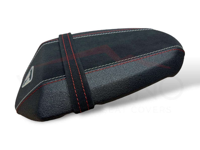 Puede incluir: Funda de asiento negra con costuras rojas y blancas. La funda tiene una superficie texturizada y una correa negra con costuras rojas. Un logotipo blanco es visible en el lateral.