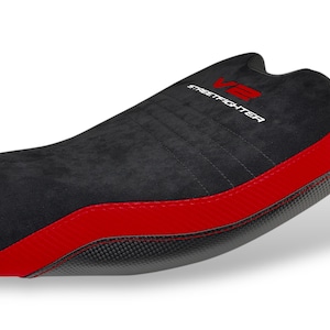 May include: Black motorcycle seat with red accents. The seat features the text "V2 STREETFIGHTER" in white and red. The seat has a textured surface and a curved design, suitable for a motorcycle.