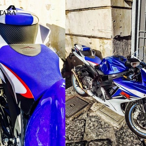 May include: A blue and white motorcycle with a custom seat featuring the Alcantara logo. The motorcycle is parked on a cobbled street.