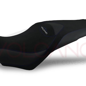 May include: Black motorcycle seat cover with blue stitching and the word "VOLCANO" in blue. The seat cover has a sleek, contoured design, and is likely made of a durable, weather-resistant material.