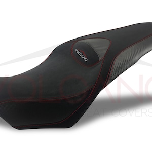 May include: Black motorcycle seat cover with red stitching and a gray carbon fiber panel. The seat cover has the word "VOLCANO" embroidered on it.