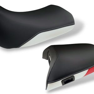 Puede incluir: Dos asientos de motocicleta. Los asientos son negros con detalles blancos y de color. Uno tiene una base blanca y el otro una base blanca con rayas rojas, blancas y azules. Ambos asientos tienen costuras blancas.