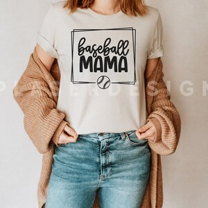 May include: A white t-shirt with a black graphic that says "baseball mama" in a box with a baseball inside the box.