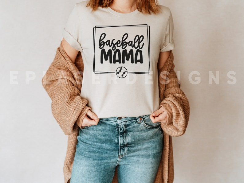 May include: A white t-shirt with a black graphic that says "baseball mama" in a box with a baseball inside the box.