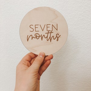 May include: A round wooden sign with the text "SEVEN months" engraved on it.