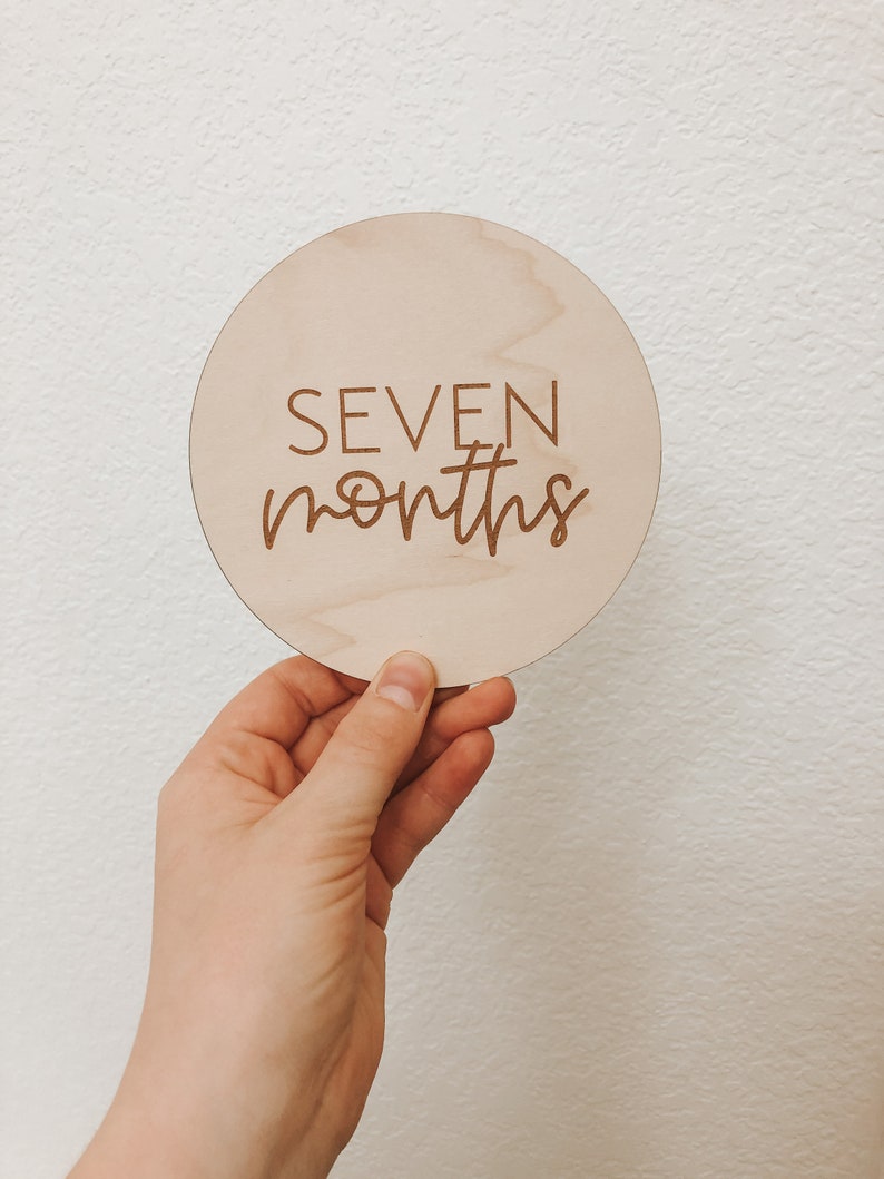 May include: A round wooden sign with the text "SEVEN months" engraved on it.