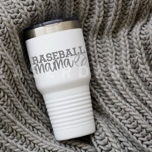 Op de afbeelding: Een witte roestvrijstalen beker met een grijze baseball en de tekst "Baseball mama" erop. De beker staat op een grijs gebreid deken.