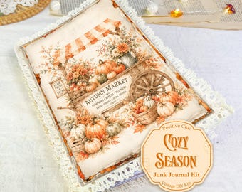 May include: A rectangular junk journal kit featuring an autumn market illustration with pumpkins, apples, and flowers. The cover is bordered by white lace trim and includes a beige label with the text Positive Chic COZY SEASON Junk Journal Kit.