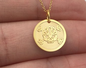May include: Gold necklace with a round pendant featuring a detailed sugar skull design. The pendant is surrounded by four smaller circles with floral designs.