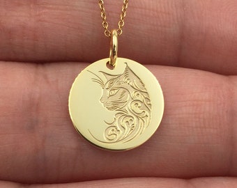 May include: A gold-colored pendant necklace featuring a circular charm with an engraved cat profile. The cat design is detailed with swirling patterns. The necklace has a delicate chain and a small loop for the chain to pass through.