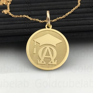 May include: A gold necklace with a round pendant featuring a graduation cap and the Greek letters Alpha and Omega.