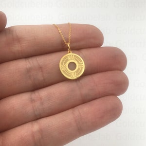 May include: A gold-colored pendant necklace. The pendant is circular with Roman numeral markings and a central design. The necklace chain is delicate and also gold-colored. The jewelry is held in a hand.