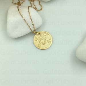 May include: A gold chain necklace with a round pendant featuring a detailed sugar skull design. The pendant is on a white background.